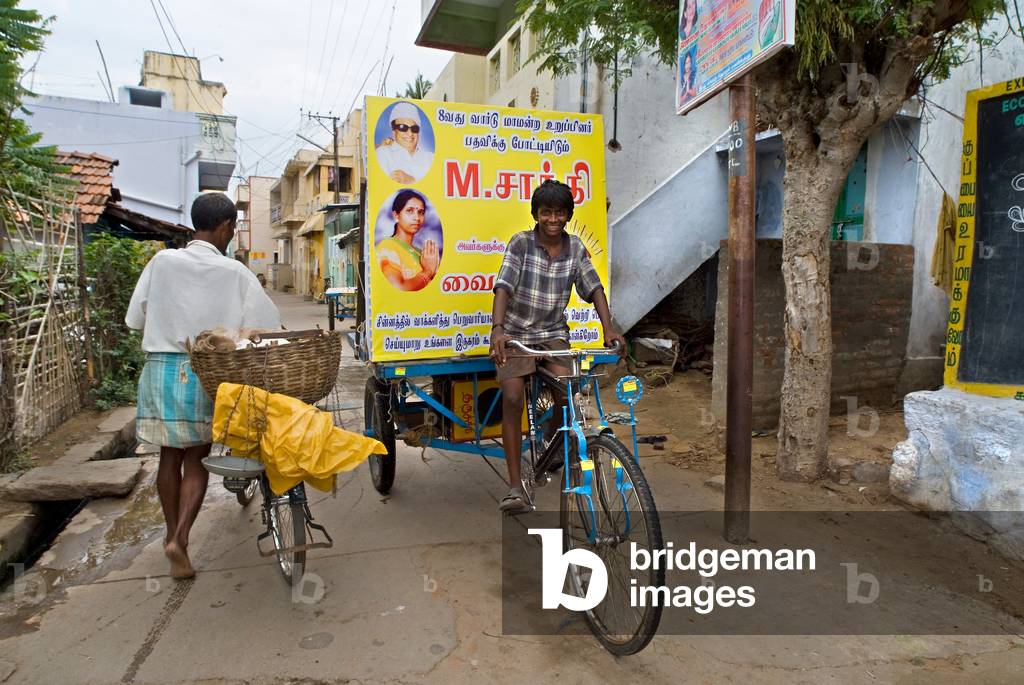 Boy on poster-bike in narrow street canvassing for party political elections (photo)