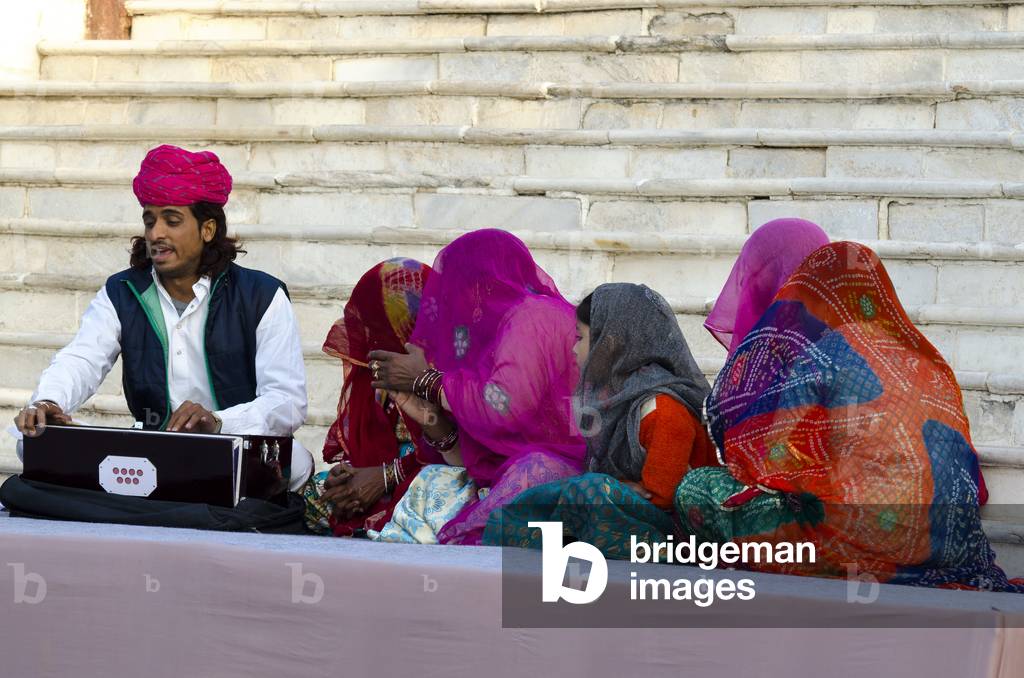 Turbaned Indian harmonium player & group of colourfully dressed veiled women with young girl chanting traditonal Western Rajasthani songs,
Jodhpur, Rajasthan, India (photo)