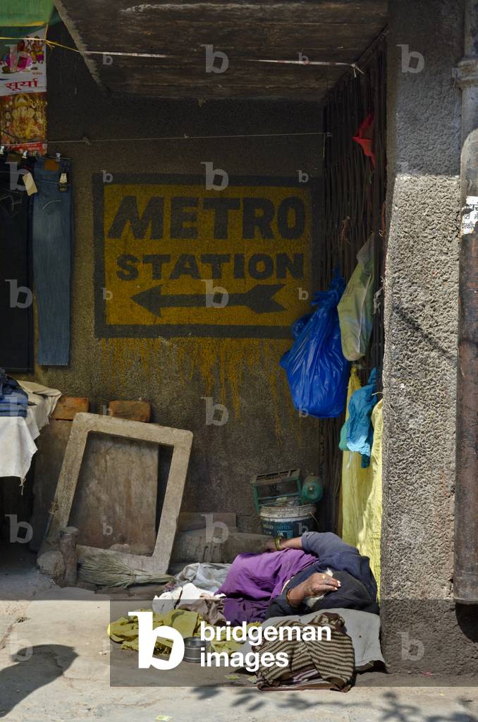 Homeless person/beggar sleeping on market street corner below 'metro' sign,
Chandni Chowk, Old Delhi, India (photo)