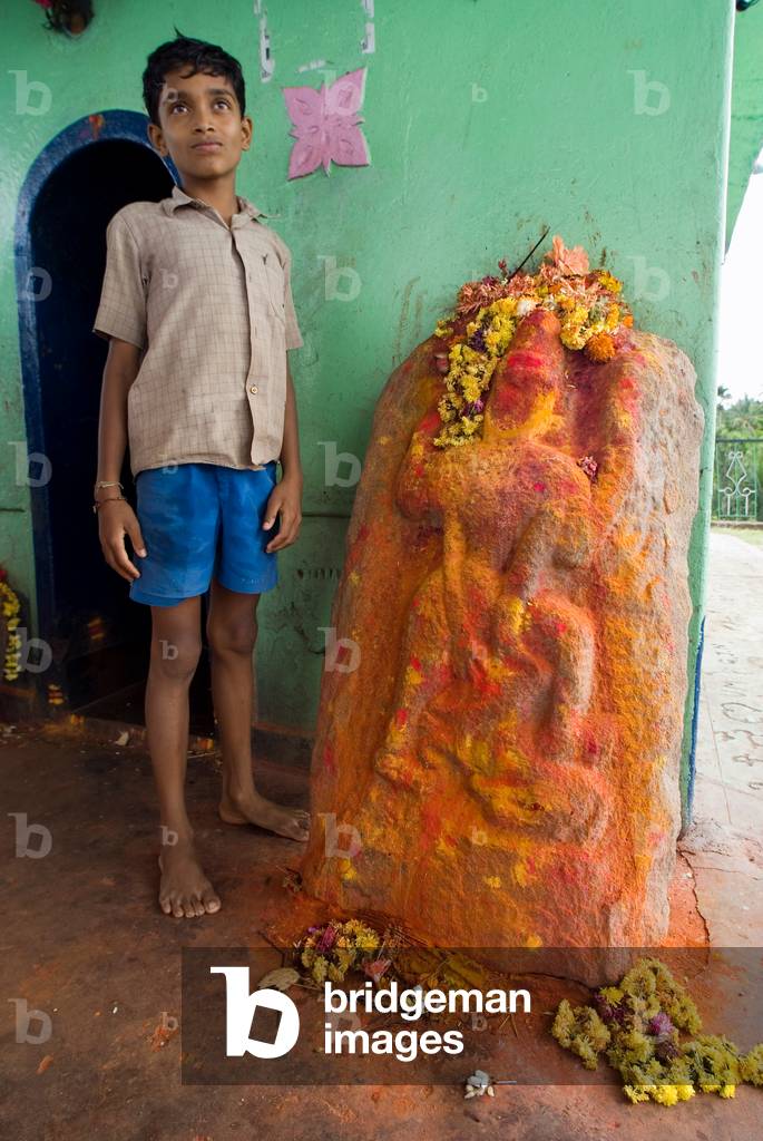Boy with a small lakeside shrine depicting the icon of Rami 
