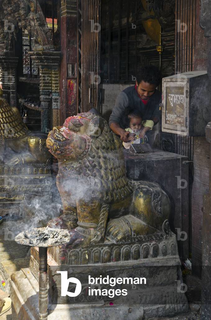 Bagh Bhairav Temple: Worshipper with young daughter making offering at temple entrance behind snow lion sculpture, Kirtipur, Kathmandu Valley, Nepal (photo)