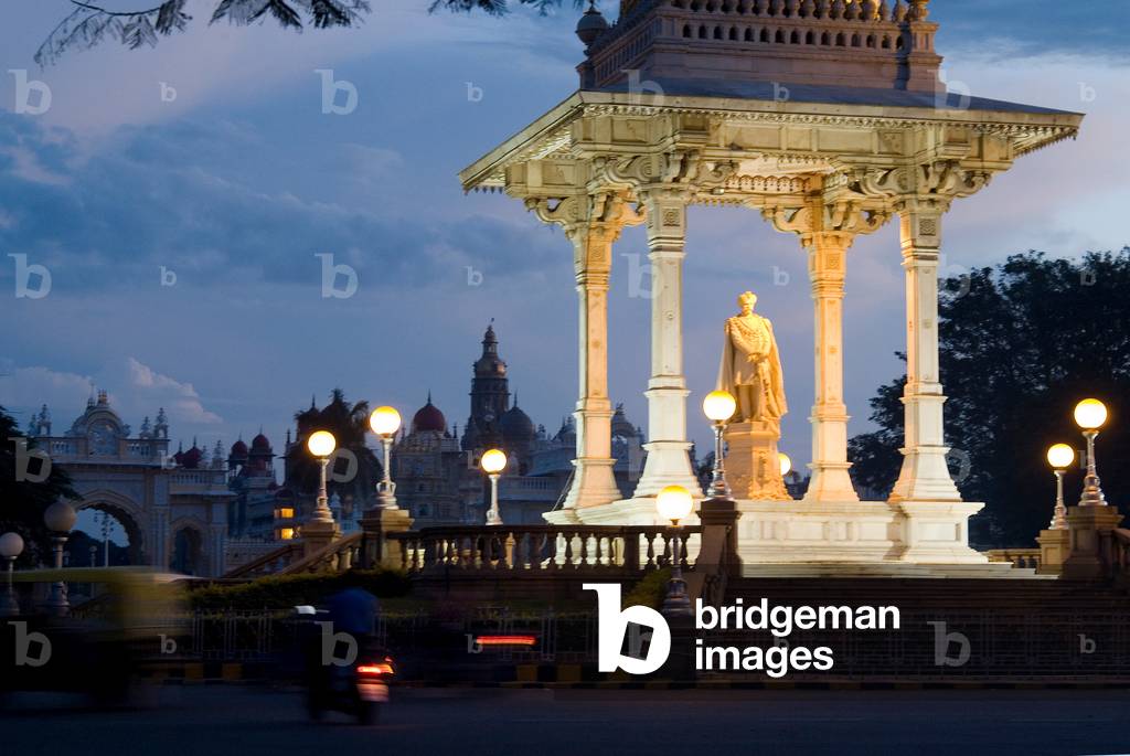 Statue of the Maharaja of Mysore illuminated at dusk with Maharaja's palace in the background (photo)