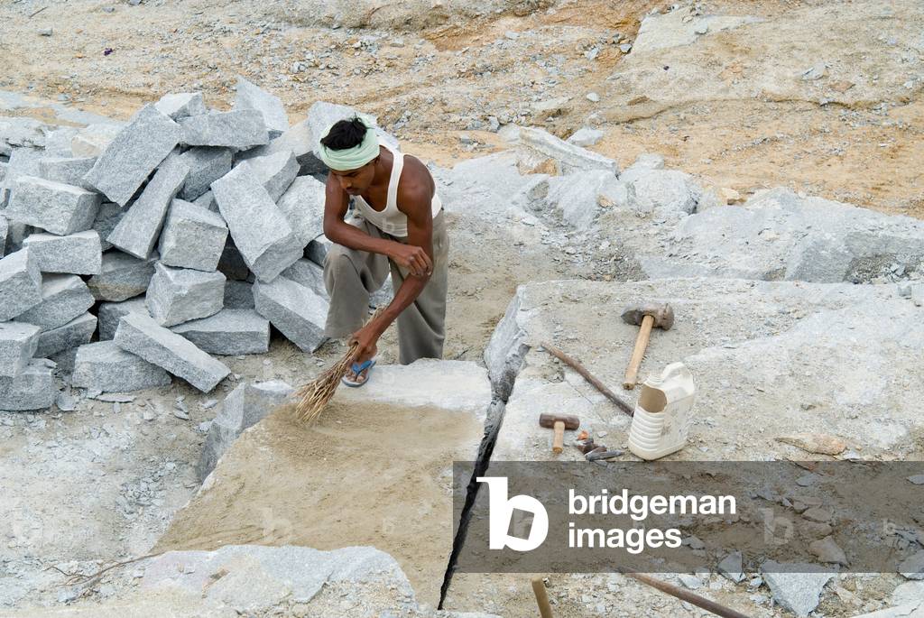 Worker in granite quarry manually splitting slabs of rock (photo)