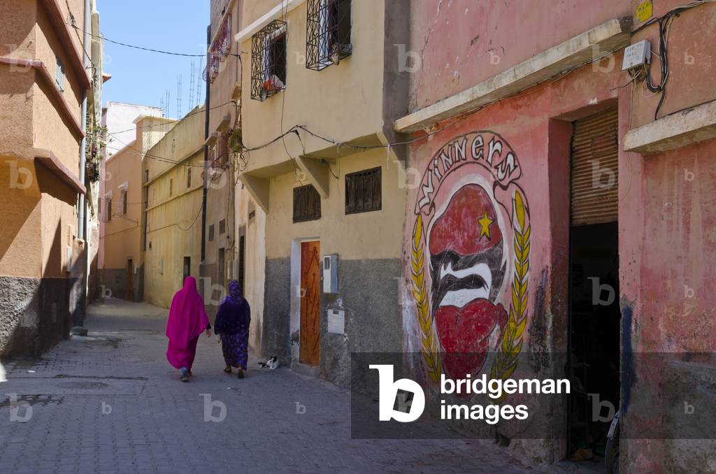 Two women in traditional robes walking through narrow medina alley in  Berber town, Taroudant, Souss-Massa-Draa Region, Morocco (photo)