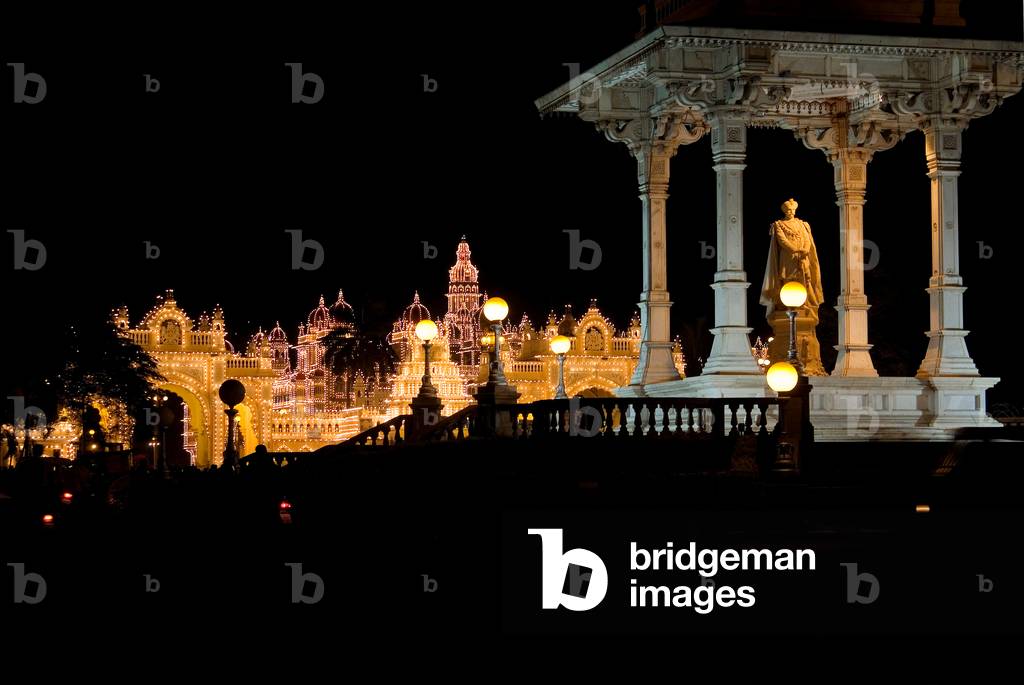 Statue of the Maharaja of Mysore illuminated at dusk with Maharaja's palace in the background (photo)