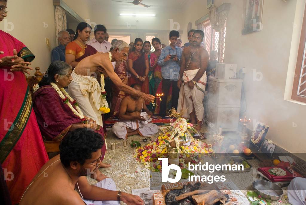 old couple performing special Vedic ceremony on combined occasion of 50th wedding anniversary and 80th birthday with priests and family in living room (photo)