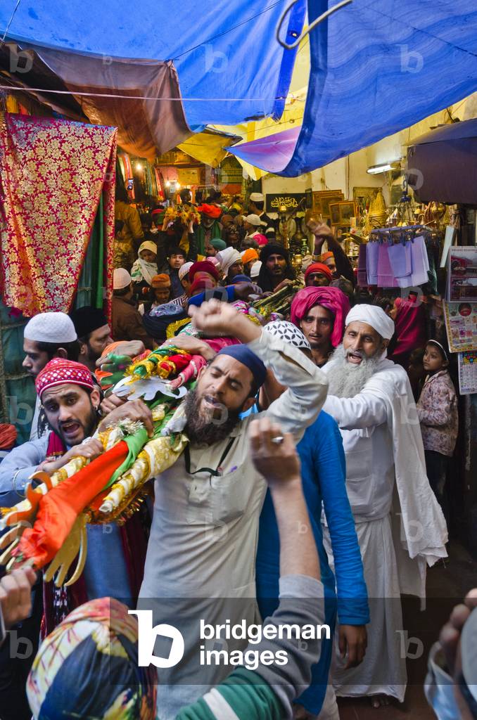 Sufi devotees carrying rolled up Sufi flags through a busy bazaar alley leading to the shrine and tomb of Nizamuddin, New Delhi, India (photo)