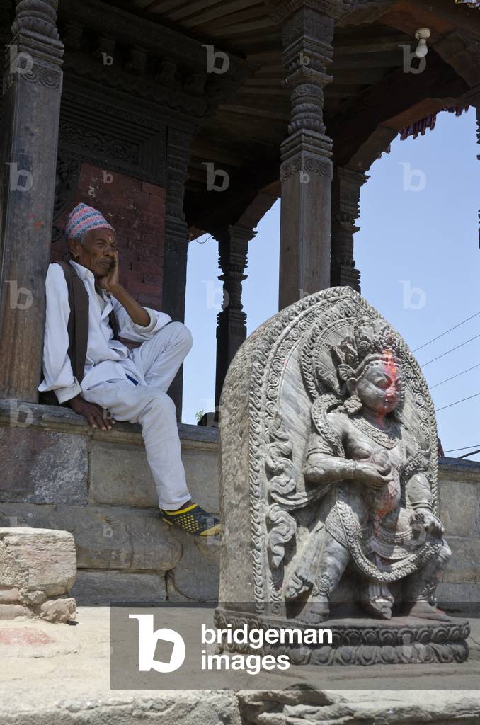 Nepali man resting in temple shade behind sculpture of Bhimsen, Uma Maheshwar Temple, Kirtipur, Kathmandu Valley, Nepal (photo)