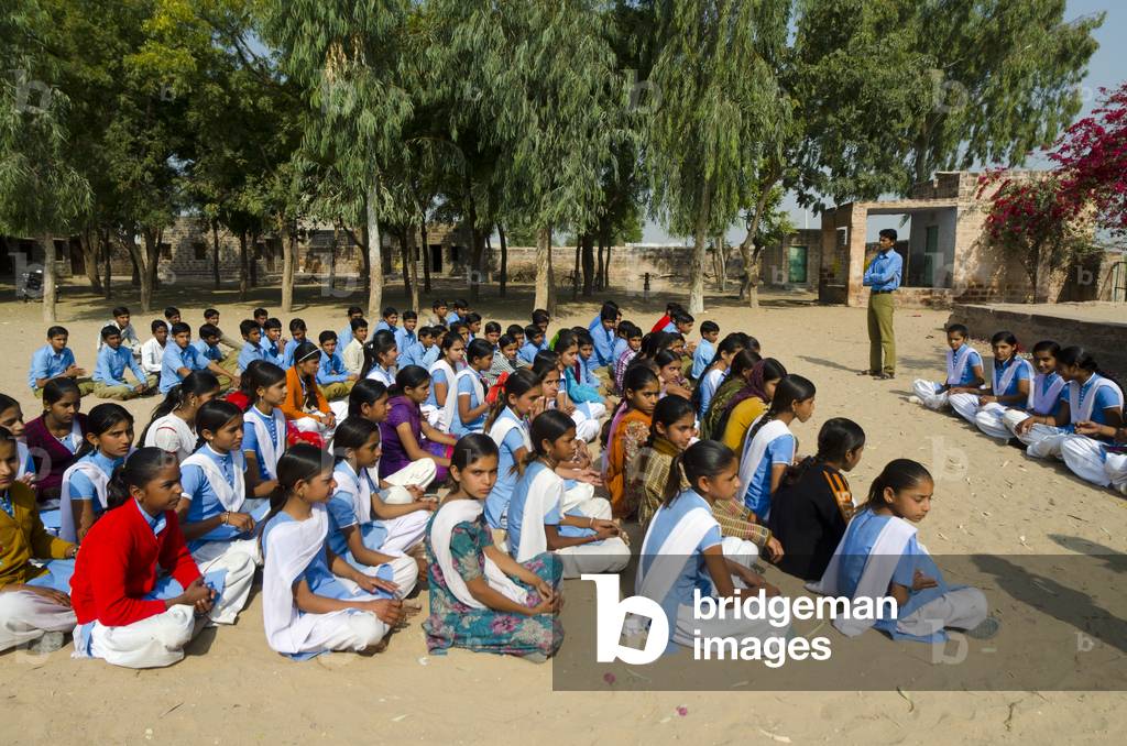 Pupils sitting on ground in schoolyard during morning assembly,
Gagadi (aka. Gagari) village, Rajasthan, India (photo)