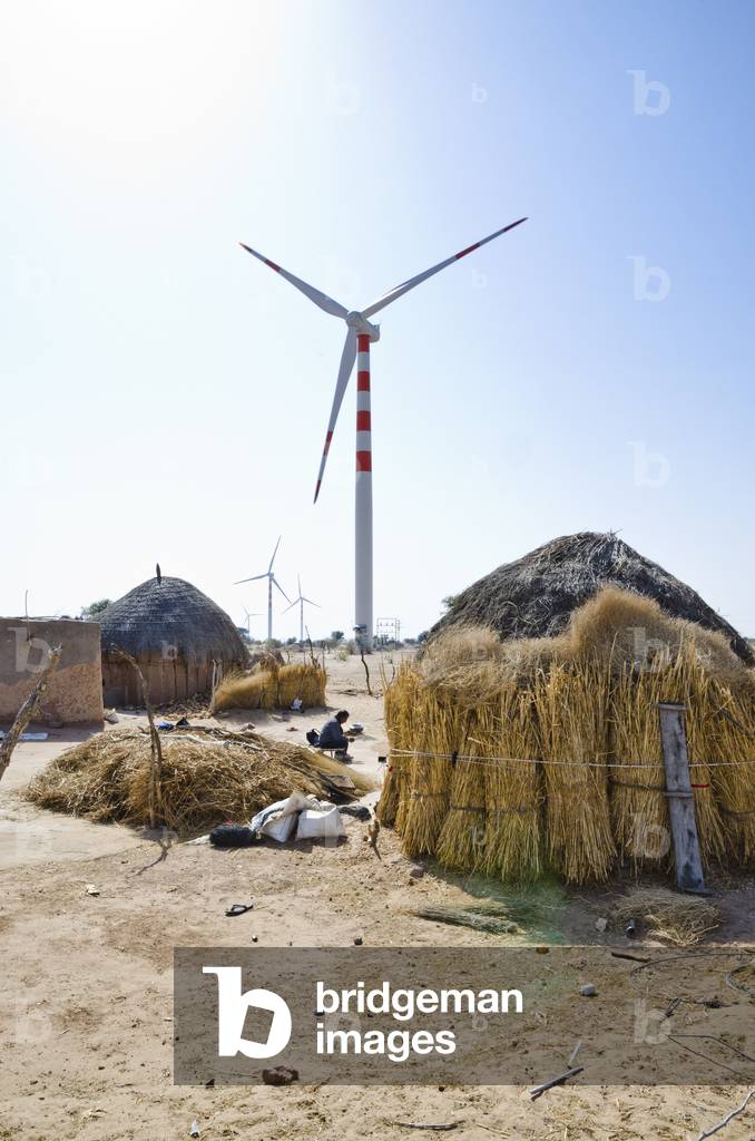 Wind turbines behind traditional huts in a Thar Desert village, Lakhmana, Rajasthan, India(photo)