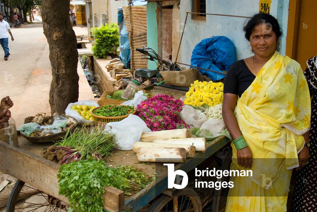 Mobile greengrocer and flower seller with her cart on a street corner in Vidyaranyapura, Bangalore, Karnataka, India

