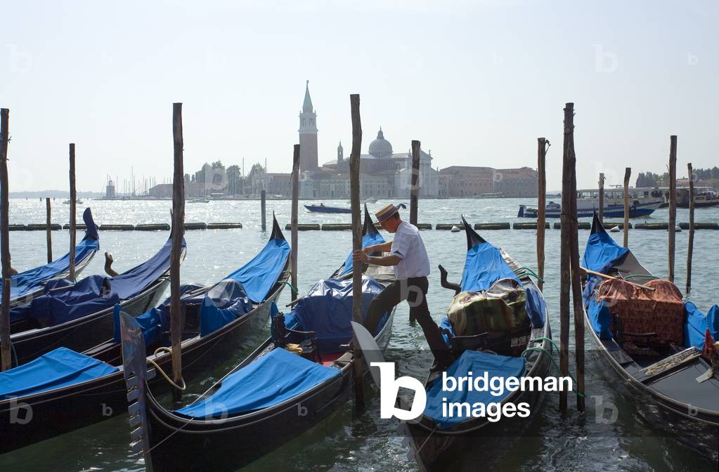 Gondolier steps across to his Gondola in the early morning in Venice, (photo)