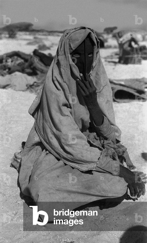 Portrait of a woman of the Harasis Bedouin sitting on the ground in the region between Boi well and Yisub well in the Jiddat al Harasis, Oman, February 4–14, 1947 (b/w photo)