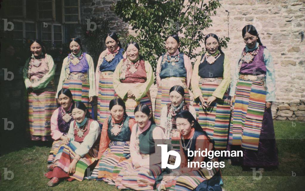 Group portrait of thirteen aristocratic Tibetan women, standing and sitting on the ground, wearing colourful silk dresses and aprons, Lhasa, Tibet, March 1945 – early 1949 (colour transparency)