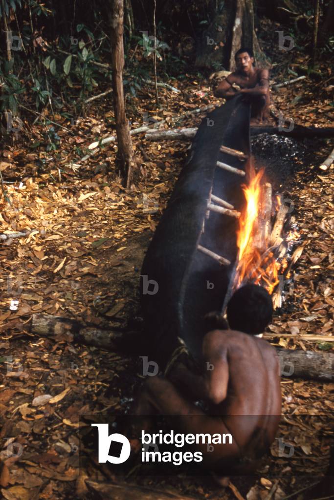 Tukano men heating a canoe over a fire so the sides can be forced apart, Piraparaná River, Vaupes department, Colombia, 1960-61 (photo)