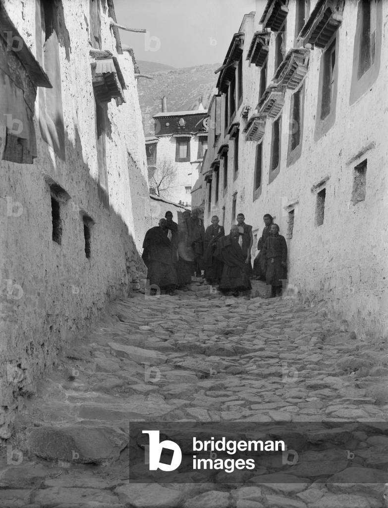 A lane in Drepung Monastery with a group of monks gathered in the middle distance, c.1920-21 (glass plate gelatin print)