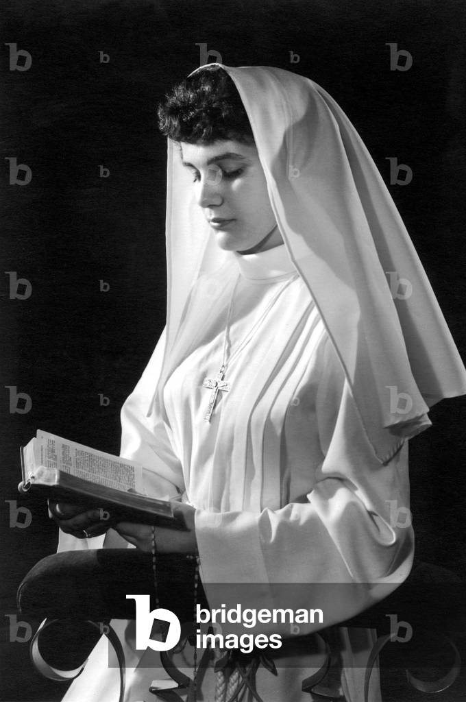 Young woman wearing alb, veil and cross, reading Bible for her solemn declaration of faith made at the age of 11 c. 1965