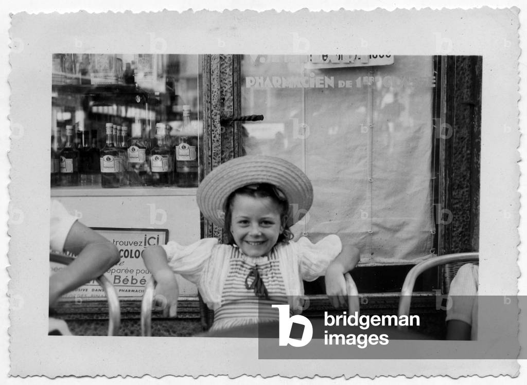 Young girl smiling, seated at a cafe during summer holidays, France, c. 1950 (b/w photo)
