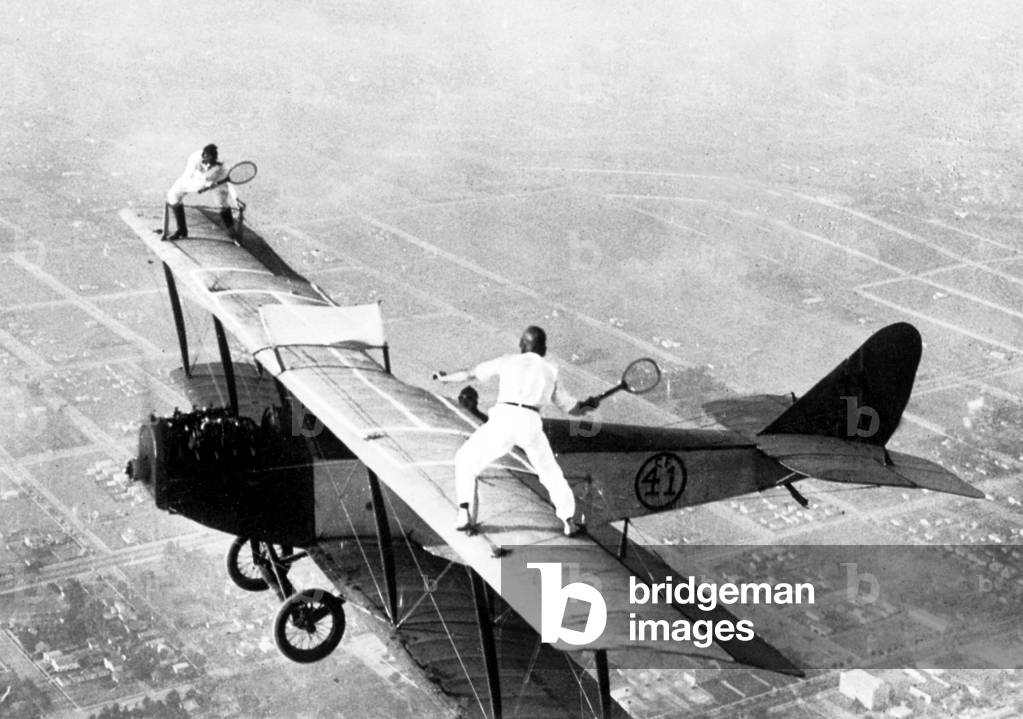 Ivan Unger and Gladys Roy playing tennis on flying plane 1925 (b/w photo)