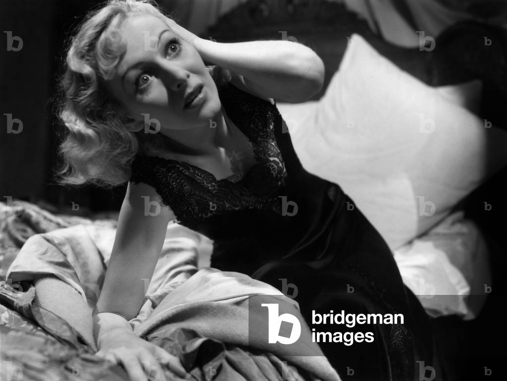 Woman on a bed, straining her eyes because of fear, 50's