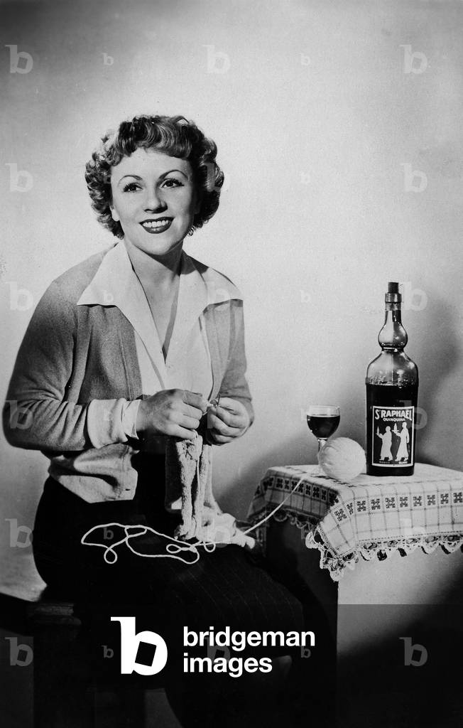 Odette Laure (1917-2004) french comedian, knitting (bottle of St Raphael aperitif) c. 1950
