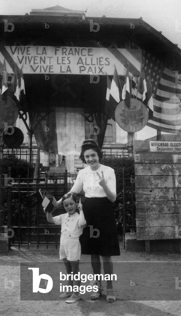 A mother and her child holding french, soviet and american flags, celebrating end of war, France, september 1945