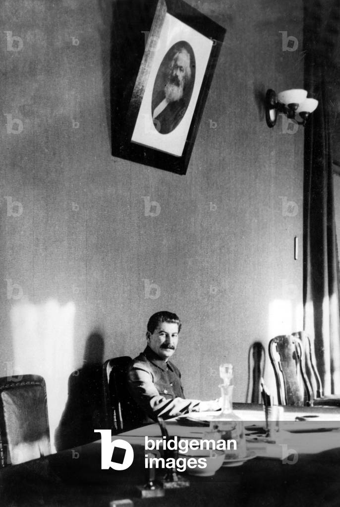 Joseph Stalin (1879-1953) russian politician here in his office, on the wall KarlMarx's portrait, c. 1945