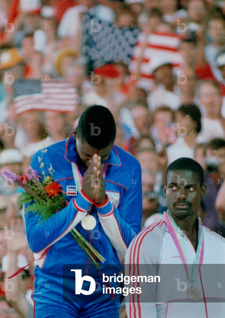 Image of CARL LEWIS PRAYS AFTER BEING PRESENTED GOLD MEDAL FOR WINNING