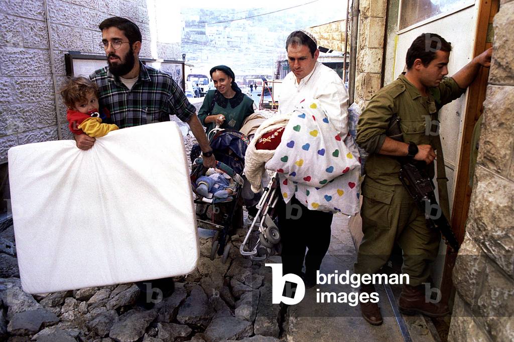 Image of A Jewish settler family carrying their children and bedding pass