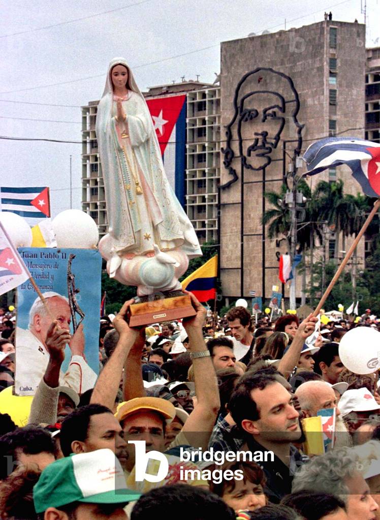 Worshipers hold up a statue of the Virgen Mary, Pope posters, and Cuban flags beneath a facade of Ch.., 1998-0