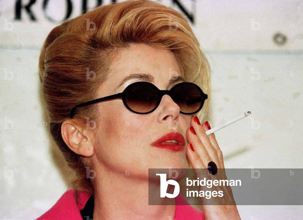 Image of French actress Catherine Deneuve holds a thin cigarette in her