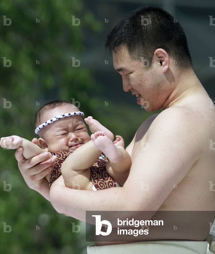 Image of An amateur sumo wrestler smiles at a weeping baby during