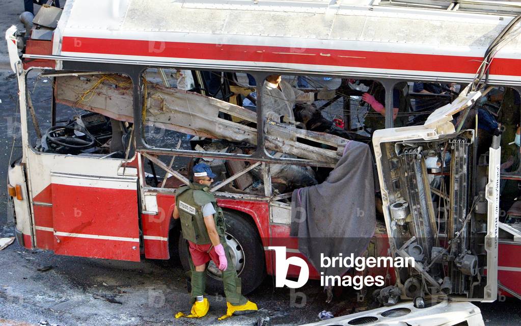 Image of ISRAELI POLICEMAN SEARCHES BUS DESTROYED BY SUICIDE BOMING IN