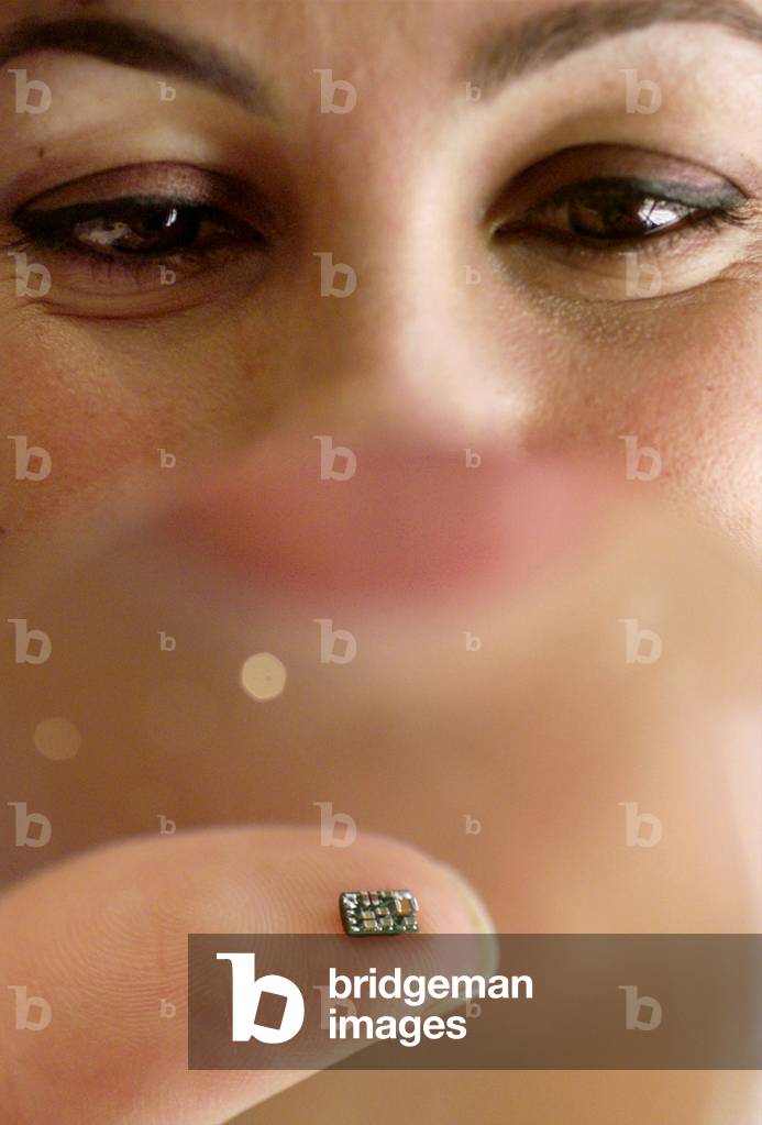 Mimi Farah holds through a magnifying glass the world's smallest microchip ever designed for a heari.., 1999 (photo)