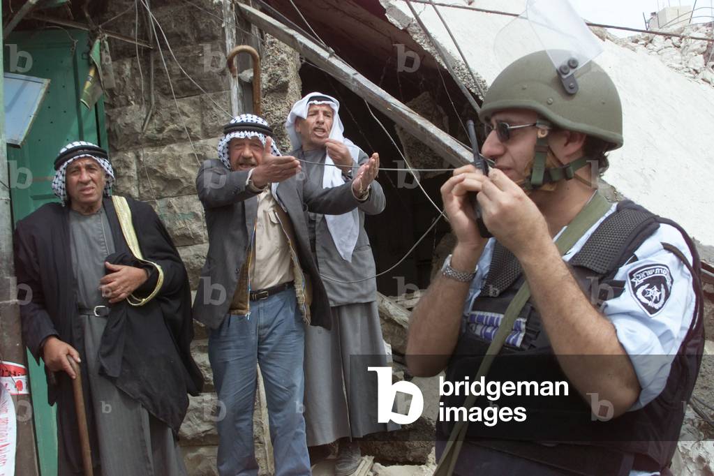 PALESTINIANS IN FRONT OF THEIR DEMOLISHED STORES SHOUT AT ISRAELI POLICEMAN IN HEBRON, 2001-04-02 (photo)