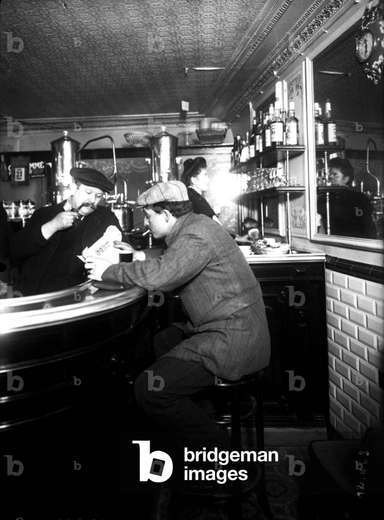 Man seated at a cafe counter reading a sports newspaper, 1911 (b/w photo)