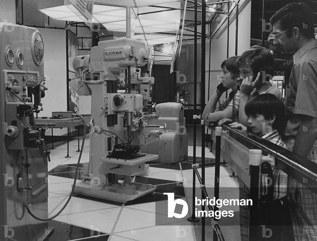 A Man And Three Boys Looking At A Display Of Various Machine Tools