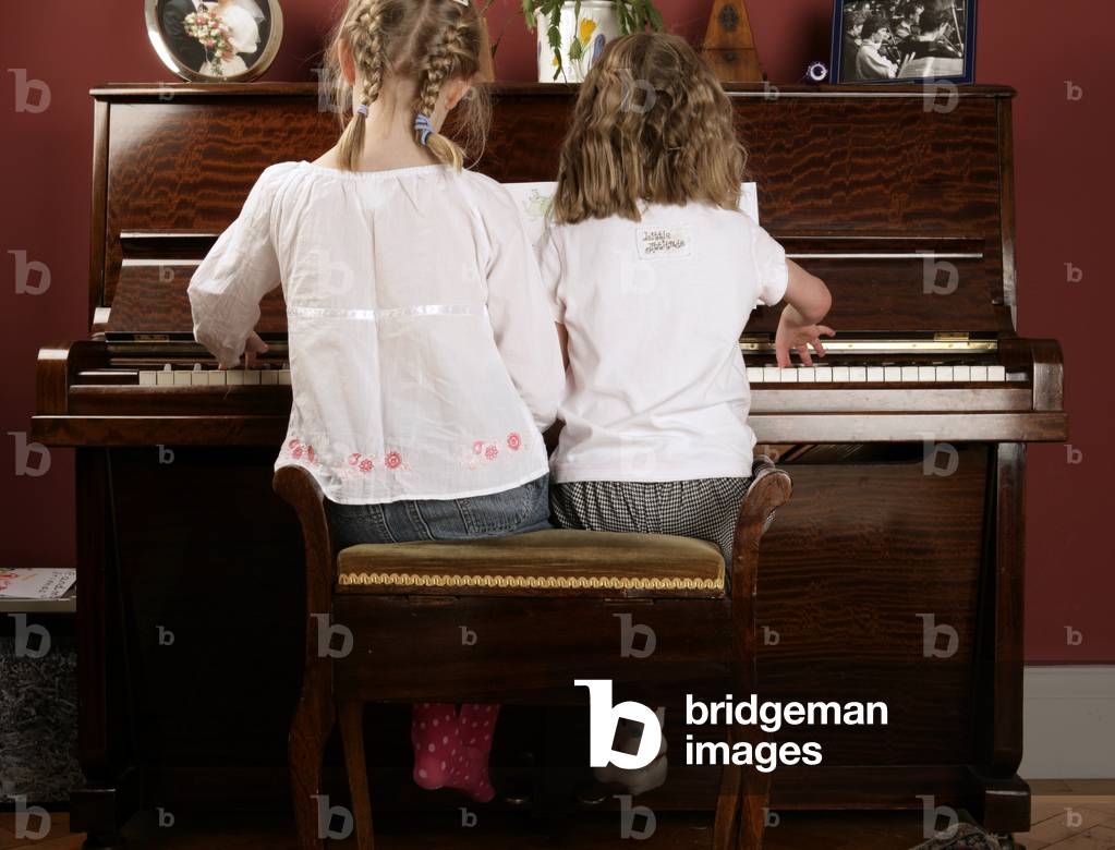 Two young girls playing the piano together.