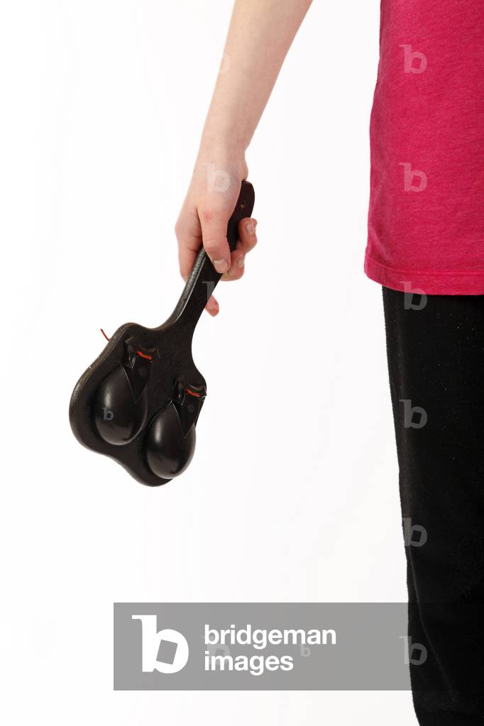 Child playing handle, board, or paddle castanets. Two castanets mounted on either side of a board. Castanets made by Elton. Gneric