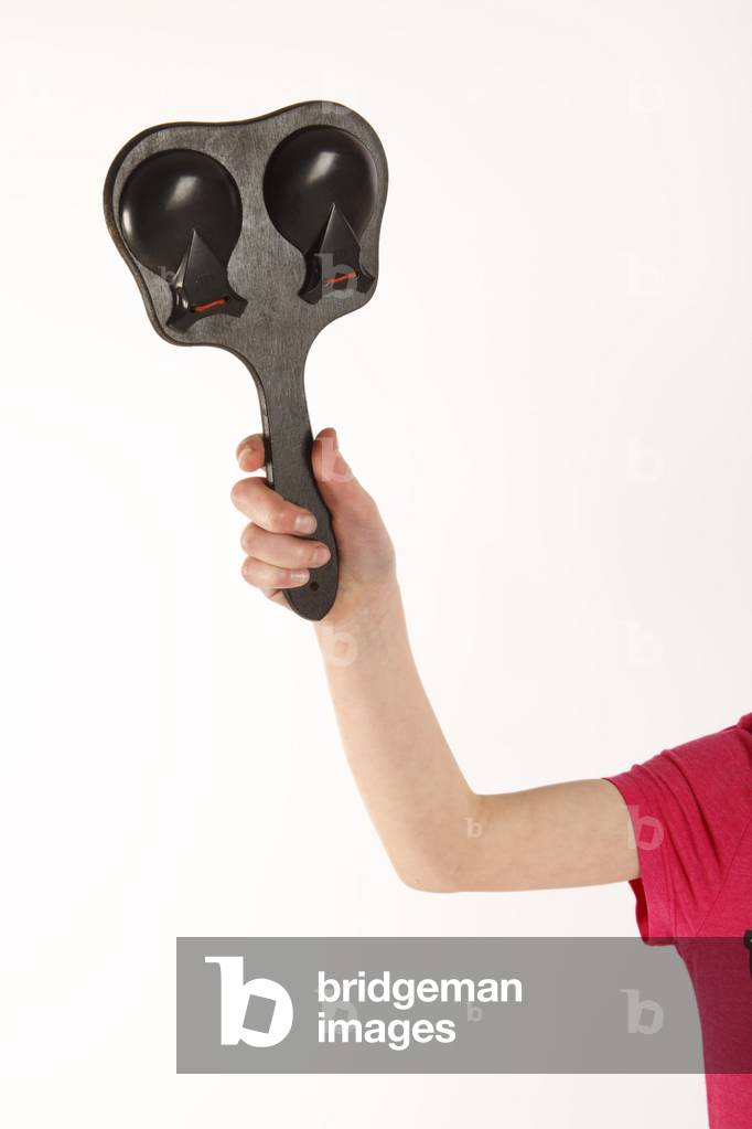 Child playing handle, board, or paddle castanets. Two castanets mounted on either side of a board. Castanets made by Elton. Gneric