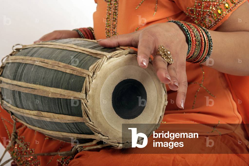 Mridangam - portrait of a young Indian woman playing an Indian hand drum made from a wooden shell, with natural skin heads of differing sizes at either end.