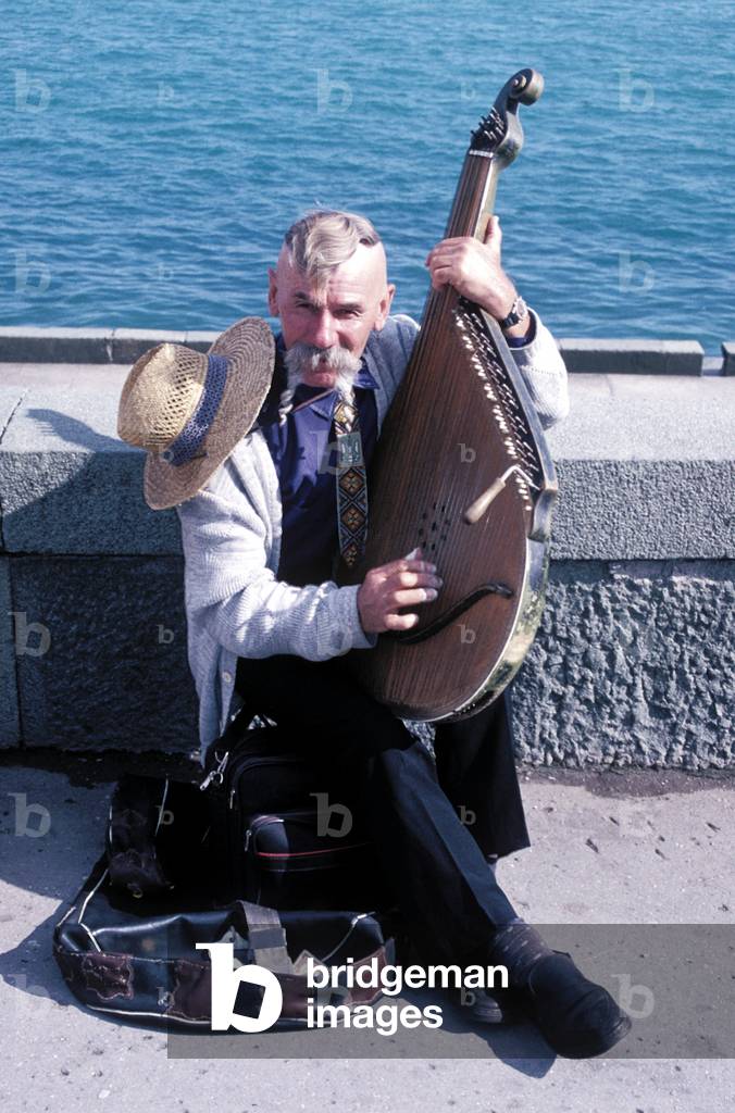 Ukrainian holding traditional string folk instrument by seafront, Yalta, Ukraine