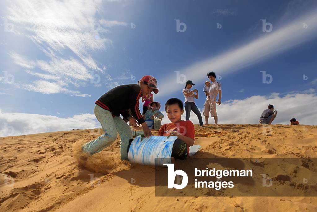 Young people having fun throwing themselves through the desert sand at the White Sand Dunes, Mui Ne, Vietnam (photo)