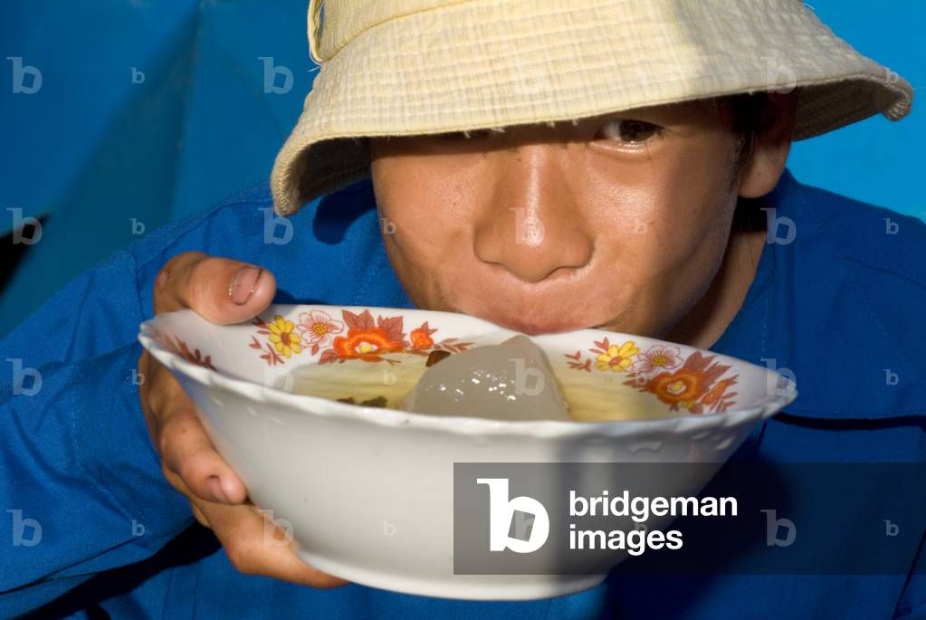 Smiling Vietnamese man wearing a Vietnamese helmet and drinking ice tea, Dien Bien Phu, Vietnam, Asia (photo)