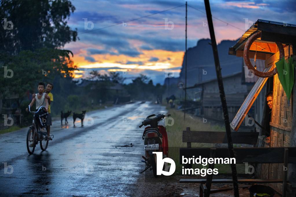 Boys with a bicycle on main street at night in Hinboun, Bolikhamsai Province, Laos (photo)