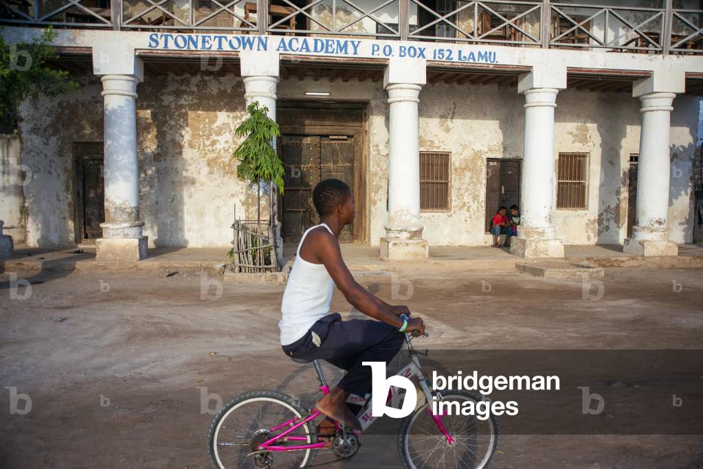 Men riding on a bicycle on the main street of Lamu town in Lamu Island, Kenya, 2020 (photo)