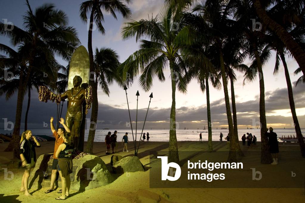 Toursists at night in front of the statue of Duke Kahanamoku, the father of surf who popularized the sport, Waikiki Beach, O'ahu, Hawaii (photo)