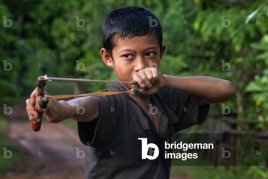 Boy playing with a slingshot in a rural aera in Thakhek village in Hinboun District Khammouane, Province, Laos (photo)