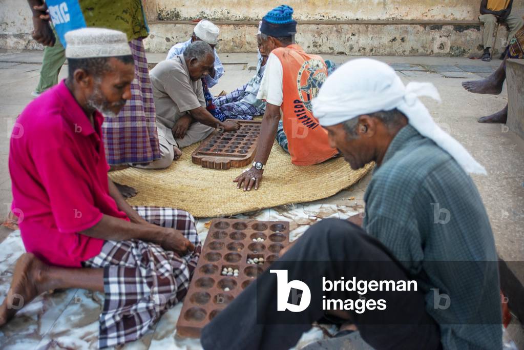 Group of Musilm men playing awale or Bao wearing traditional clothes enjoy leisure time in Lamu island town, 2020 (photo)