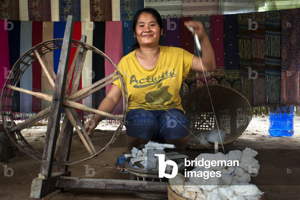 Local woman uses traditional techniques to spin wool onto a wooden Spinning Wheels a village in, Laos (photo)